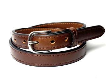May include: A brown leather belt featuring a smooth finish, tonal stitching along the edges, and a silver-toned metal buckle. The belt is coiled into a circular shape, displaying multiple punched holes for adjustment and a single leather keeper loop.