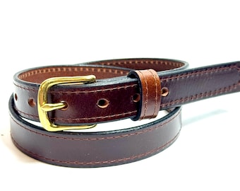 May include: A dark brown leather belt featuring a smooth finish, visible tonal stitching along the edges, and a polished gold-tone metal buckle. The belt is coiled, showing multiple punched holes for adjustment and a matching leather keeper loop.