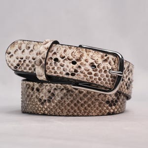 May include: A rolled snakeskin belt with a silver-colored buckle. The belt features a pattern of beige and brown scales. The buckle is rectangular and has a single prong. The belt is a fashion accessory.