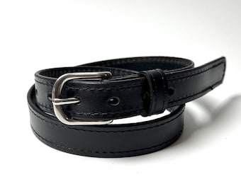 May include: A black leather belt featuring a silver-toned metal buckle and a single matching leather keeper loop. The belt has visible stitching along the edges and multiple punched holes for adjustment, coiled into a circular shape.