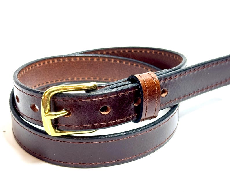 May include: A dark brown leather belt featuring a smooth finish, tonal stitching along the edges, and a polished gold-tone metal buckle. The belt is coiled, showing a single leather keeper loop and multiple circular adjustment holes.