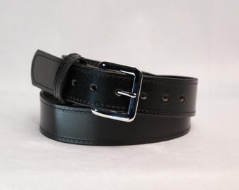 May include: A black belt featuring a smooth, polished finish with tonal stitching along the edges. The belt includes a rectangular silver-toned metal buckle and a series of circular adjustment holes punched along the length of the strap.