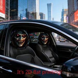 May include: Two car headrest covers featuring a graphic print of a hooded, pale-skinned creature with glowing red eyes and sharp fangs. The covers are black with a textured pattern on the lower section. The text It's 2D flat printing is visible.