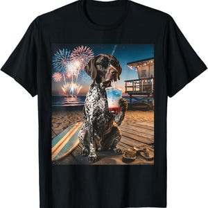 Pode incluir: Camiseta preta com um cão de caça alemão usando óculos de sol e segurando uma bebida, com um cenário de praia com fogos de artifício. Uma prancha de surf e sandálias também estão presentes.