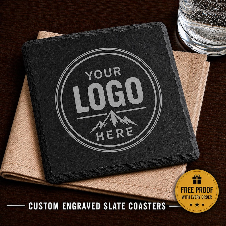 May include: A square black slate coaster with rough, natural edges. The center features a circular engraved design with the text "YOUR LOGO HERE" above a mountain graphic. A gold circular sticker in the corner reads "FREE PROOF WITH EVERY ORDER."