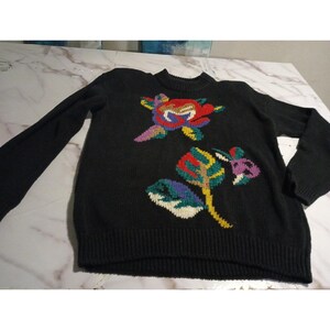 May include: Black knit sweater with a crew neck and long sleeves. The sweater features colorful floral embroidery in red, yellow, green, blue, and purple. The flowers are placed on the front of the sweater.