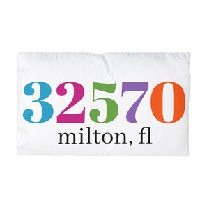 Puede incluir: Funda de almohada blanca con los números "32570" en azul, rosa, verde, morado y naranja. Debajo de los números, el texto "milton, fl" está impreso en negro.
