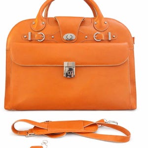 Könnte beinhalten: Eine orangefarbene Lederaktentasche mit einem oberen Griff, einer Frontklappe und silberfarbener Hardware. Enthält einen abnehmbaren Schultergurt, ein Gepäckanhänger und einen Schlüssel. Die Aktentasche hat eine abgerundete Oberseite und eine rechteckige Vordertasche.