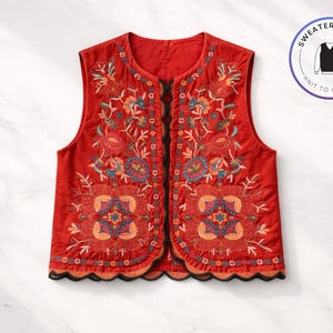 Puede incluir: Un chaleco rojo con intrincados bordados florales en tonos naranja, azul y verde. El chaleco tiene un dobladillo festoneado con ribete negro. Un gráfico redondo dice "Sweater & Vest".