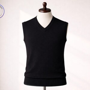 Op de afbeelding: Een zwarte V-hals trui vest getoond op een mannequin. Het vest heeft een geribbelde zoom en een klassiek ontwerp. De afbeelding bevat een logo met de tekst "Sweater & Vest" en "knit to impress".