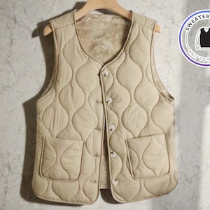 Può includere: Un gilet trapuntato beige con scollo tondo e due tasche frontali. Il gilet ha una chiusura con bottoni e un interno morbido e soffice. Il gilet è appeso a una gruccia di legno. L'immagine include una grafica circolare che dice "Sweater & Vest" e "Knit to Impress."