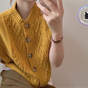 Pode incluir: Colete de malha canelada amarelo mostarda com decote em V e fecho de botões. O colete tem um design clássico de malha canelada e é sem mangas. Os botões são da mesma cor. Parte da coleção "Sweater & Vest".