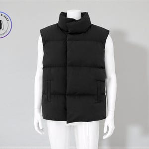 Puede incluir: Un chaleco acolchado negro con cuello alto y dos bolsillos laterales, exhibido en un maniquí blanco. La imagen incluye un logotipo circular que dice "Sweater & Vest" y "Knit to Impress".
