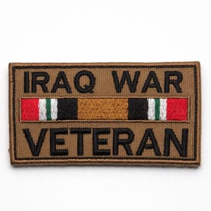 May include: A rectangular brown patch embroidered with the words "IRAQ WAR VETERAN" in black. A central ribbon features red, white, green, and black stripes. The patch is designed for military or veteran recognition.