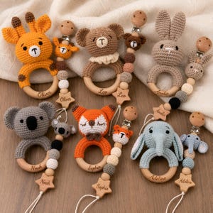 May include: Six crocheted animal rattles with wooden rings and matching pacifier clips. The set includes a giraffe, bear, rabbit, koala, fox, and elephant, each personalised with names like Oliver, Leo, Amelia, Noah, Sophia, and Adeline.