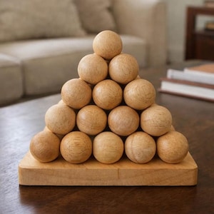 Può includere: Una scultura piramidale in legno composta da quindici sfere di legno disposte su una base rettangolare in legno. Le sfere e la base sono di colore marrone chiaro, esposte su un tavolo marrone scuro.