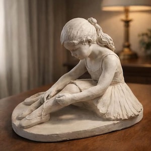 Op de afbeelding: Gedetailleerde sculptuur van een jonge ballerina die zit en haar balletschoen aanpast. De figuur zit, draagt een tutu en een eenvoudige top. De sculptuur is in een neutrale kleur en staat op een ovale basis.