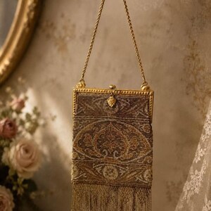 May include: A rectangular beaded handbag featuring a metallic gold frame and a matching gold chain handle. The bag is decorated with an intricate brown, gold, and tan floral pattern and finished with a long, delicate beaded fringe at the bottom.