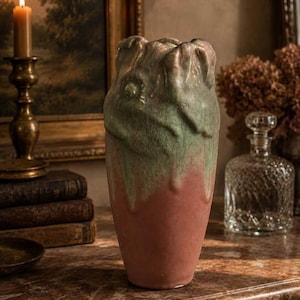 May include: A ceramic vase with a tapered cylindrical body featuring a matte terracotta base and a textured, dripped sage green glaze at the top. The rim has an irregular, organic shape with raised, sculpted folds that resemble petals.