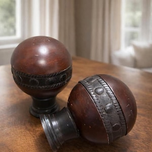 May include: Two decorative wooden spheres with dark brown finishes and black accents. Each sphere has a dark band with embossed detailing. One sphere is upright on a pedestal base, while the other is lying on its side.