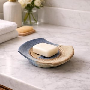 May include: A white ceramic mug with a black handle and the text "But First, Coffee" in a bold, black font. The mug is set against a blurred background, suggesting a cosy setting.