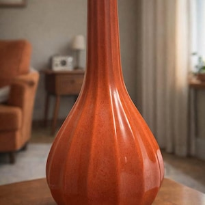 Könnte beinhalten: Eine hohe, orangefarbene Keramikvase mit strukturierter Oberfläche und vertikalem Rippendesign. Die Vase hat einen abgerundeten Boden und einen langen, schlanken Hals. Ein dekorativer Artikel, wahrscheinlich für die Inneneinrichtung.