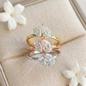 Peut inclure: Trois bagues empilées verticalement, chacune ornée de deux pierres transparentes taille poire. La bague supérieure est en or jaune, celle du milieu en or rose et la bague inférieure est en métal argenté. Chaque bague a un anneau poli.