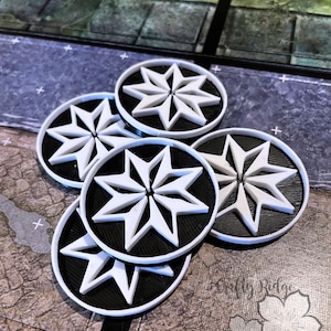 May include: A collection of five black and white game tokens. Each token features a white eight-pointed star design on a black circular base with a white border. The tokens are scattered on a game board.
