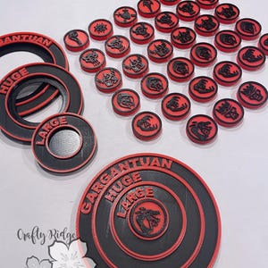 May include: Set of red and black plastic game tokens with various symbols. The tokens are arranged in a circle around a set of three black and red concentric circles with the words "Gargantuan", "Huge", and "Large" printed on them.