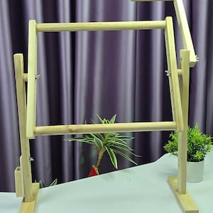 Puede incluir: Un soporte de bastidor de bordado de madera con un marco rectangular y altura ajustable. El soporte está hecho de madera clara y presenta un diseño simple y funcional. Está diseñado para sujetar bastidores de bordado.