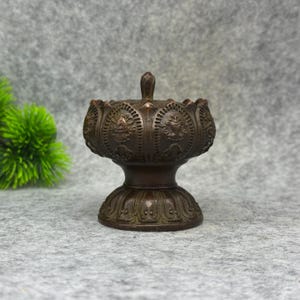 以下が含まれることがあります： 中央に突起のあるボウル型のトップと、幅広く広がったベースを備えたダークブロンズ色の金属製香炉。外側の表面には、複雑なエンボス加工のパターンと繰り返される花のようなモチーフが全体に施されています。