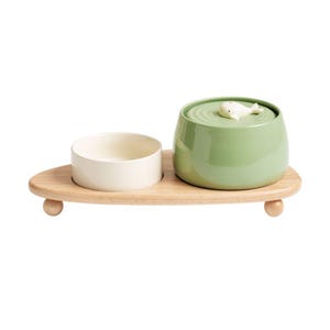 May include: A wooden serving tray with two ceramic bowls. One bowl is off-white, and the other is a light green with a whale-shaped lid. The tray has rounded wooden feet. This set is ideal for serving snacks or small portions.
