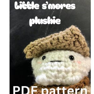 May include: A crocheted s'more plushie with a white marshmallow body, a brown biscuit-like hat, and a chocolate-coloured scarf. The text "little s'mores plushie" and "PDF pattern" are displayed in white.