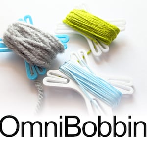 May include: Three plastic bobbins in blue and white, each wrapped with different colored thread: grey yarn, lime green thread, and light blue thread. The text OmniBobbin is printed in black at the bottom of the image.