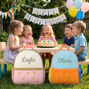May include: Two children's backpacks, one pink and the other blue, with embroidered names "Layla" and "Oliver". The pink backpack has a pineapple pattern. The backpacks are in front of a birthday party scene with children and a cake.