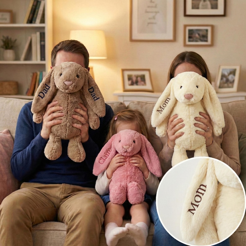 May include: Three plush bunny rabbits in beige, pink, and tan are held by people. The beige bunny has "Mom" embroidered on an ear. The tan bunny has "Dad" embroidered on its ears. The pink bunny has "Claire" embroidered on an ear.