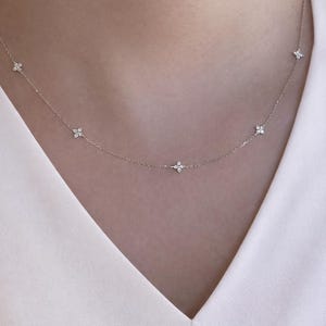 May include: A fine silver necklace with small, flower-shaped pendants. The necklace is displayed against a white top. The design is simple and elegant. A refined accessory for everyday wear or special occasions.