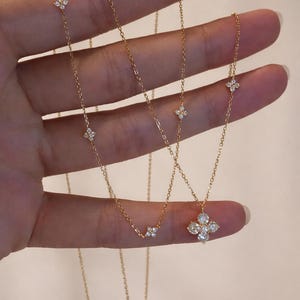 May include: Gold necklaces with diamond detailing. One necklace has a four-leaf clover pendant, others feature small diamond clusters. The necklaces are shown against a neutral background.