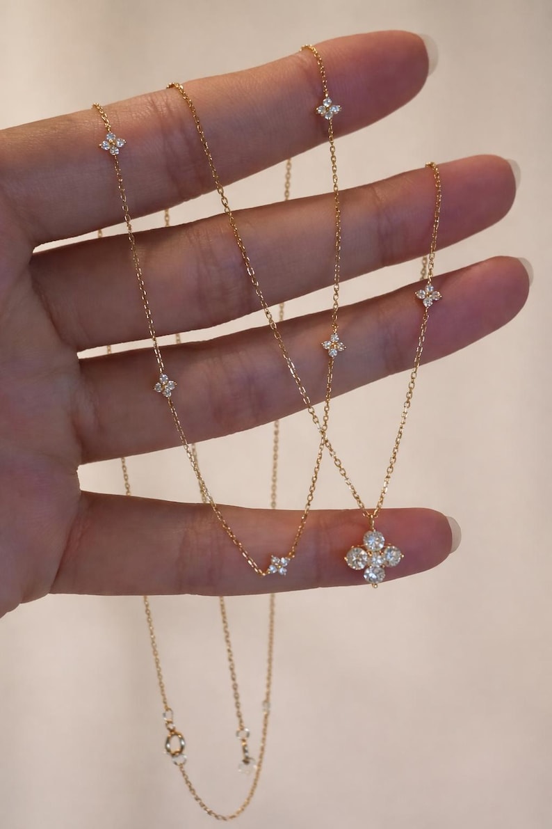 May include: Gold necklaces with diamond detailing. One necklace has a four-leaf clover pendant, others feature small diamond clusters. The necklaces are shown against a neutral background.