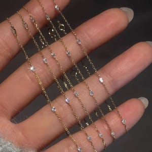 May include: Several fine gold necklaces, each adorned with small, glittering gemstones set along the chain. The necklaces are shown against a muted background, emphasising their delicate design. These necklaces are ideal for adding a touch of sparkle to any outfit.