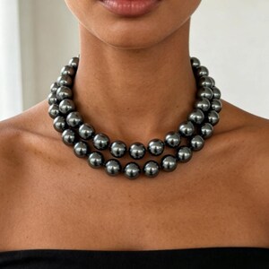 May include: A double-strand necklace featuring uniform, round, dark charcoal-gray beads with a high-gloss, reflective finish. The beads are strung together in two concentric circles that rest closely around the base of the neck.
