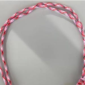 May include: A length of braided cord featuring a multi-colored pattern of pink, white, black, and grey threads. The cord is arranged in a loose loop, showcasing the intricate woven texture and the vibrant combination of these four distinct colors.