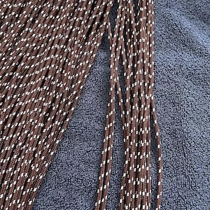 May include: A collection of brown paracord strands featuring a repeating white diagonal fleck pattern. The cords are arranged in parallel lines, showcasing the braided texture and the consistent color scheme of the individual rope segments.