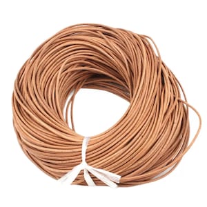 Op de afbeelding: Een strak opgerolde bundel lichtbruin lederen koord, vastgemaakt met een wit lint. Het koord lijkt een uniforme dikte te hebben en is strak opgerold, wat suggereert dat het nieuw en ongebruikt is. De neutrale kleur maakt het geschikt voor diverse knutselprojecten.