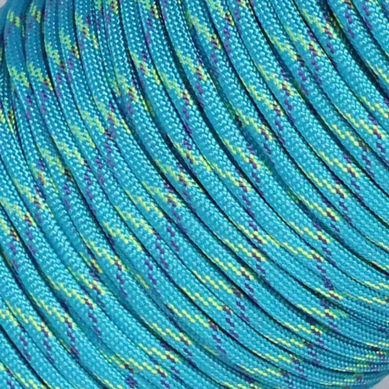 May include: A spool of braided cord featuring a vibrant turquoise base color with interwoven diagonal patterns in bright lime green and dark purple. The cord has a smooth, tightly woven texture and is coiled in parallel rows around a central core.