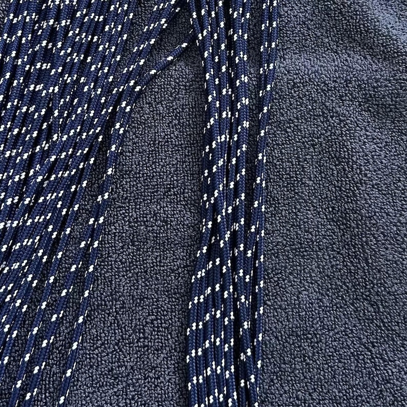 May include: A collection of multiple long, thin, braided cords in a deep navy blue color. Each cord features a repeating pattern of small, white, diagonal flecks woven throughout the length of the material, creating a consistent textured appearance.