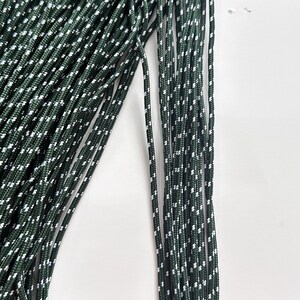 May include: A bundle of dark forest green cord featuring a repeating white speckled pattern woven throughout the length of each individual strand. The cord has a smooth, braided texture and is arranged in parallel lines against a plain background.