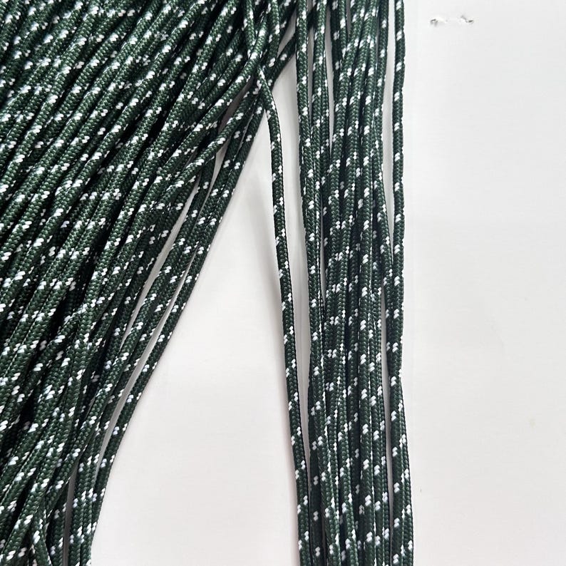 May include: A bundle of dark forest green cord featuring a repeating white speckled pattern woven throughout the length of each individual strand. The cord has a smooth, braided texture and is arranged in parallel lines against a plain background.