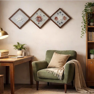 Puede incluir: Una escena interior con un escritorio de madera y una lámpara dorada, un sillón verde con un cojín y una manta beiges, y una estantería de madera. Tres obras de arte florales enmarcadas cuelgan de la pared. Las plantas en macetas añaden vegetación.