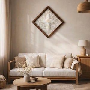 May include: A living room scene featuring a light-colored sofa with several decorative pillows. A round wooden coffee table sits in front of the sofa. A framed cross artwork hangs on the wall above the sofa. A wooden lamp and side table are also visible.